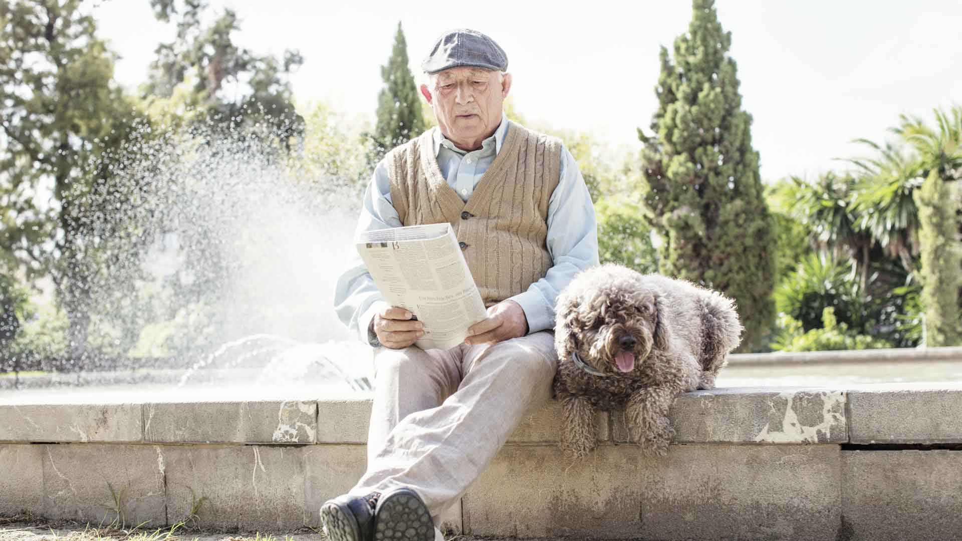 Old man reading the news paper with his dog beside him